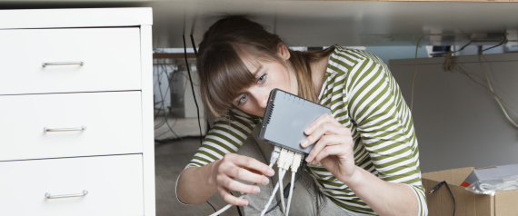 Young woman crouching under a desk connecting a modem in an office